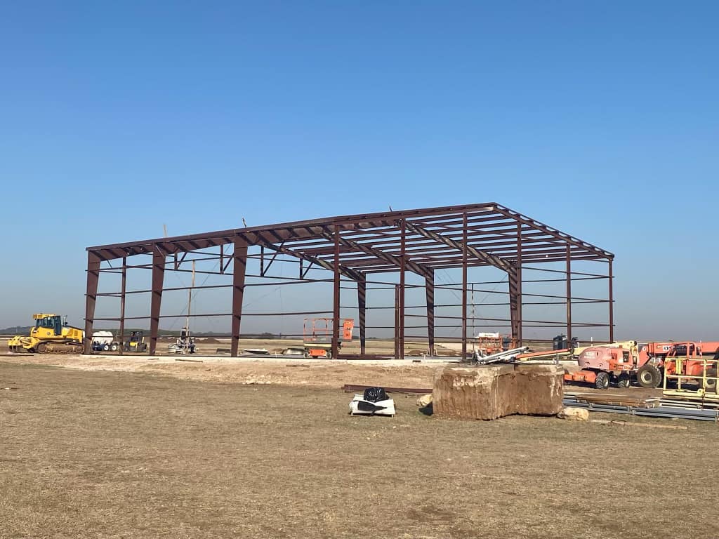Rust-primed steel building frame skeleton erected in an open Texas field before panel installation
