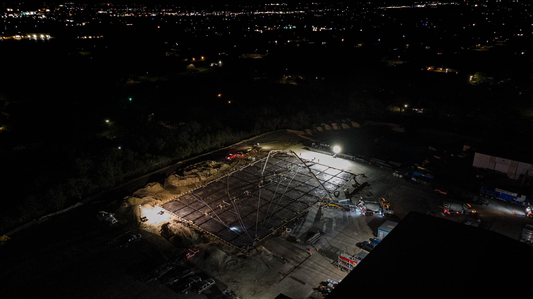 Aerial night view of a concrete foundation pour with crew and equipment on a Brazos Metal job site