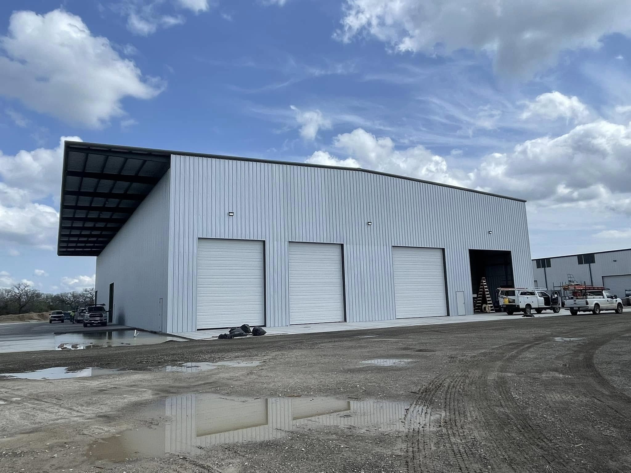 Gray commercial steel building with three garage doors and a cantilevered roof overhang
