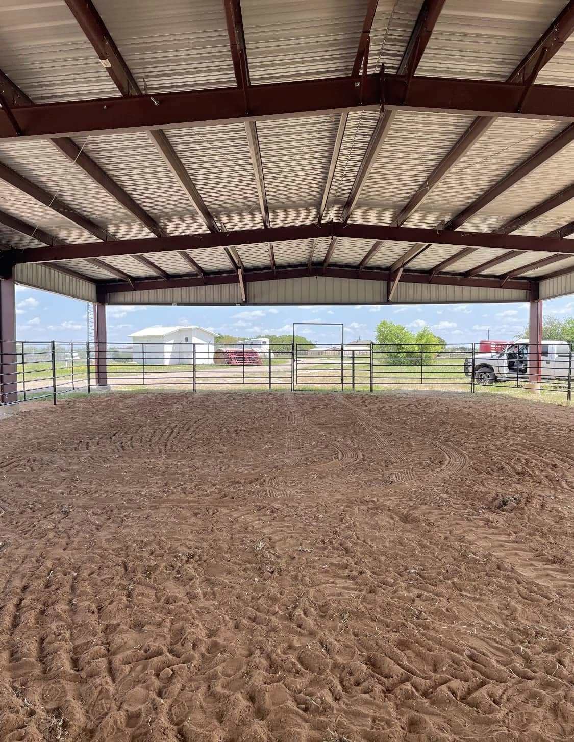 Interior of a covered horse riding arena with dirt floor and open steel-frame sides