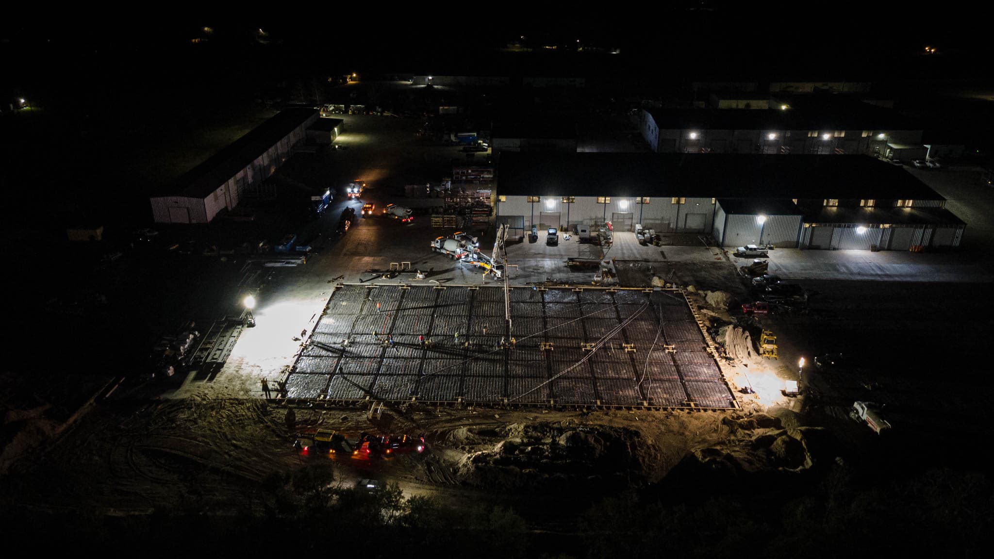Wide aerial night view of an industrial building complex lit up during active construction