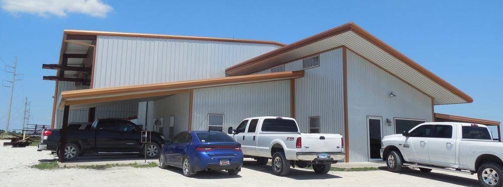 Tan metal building with orange trim and covered carport with work trucks parked in front