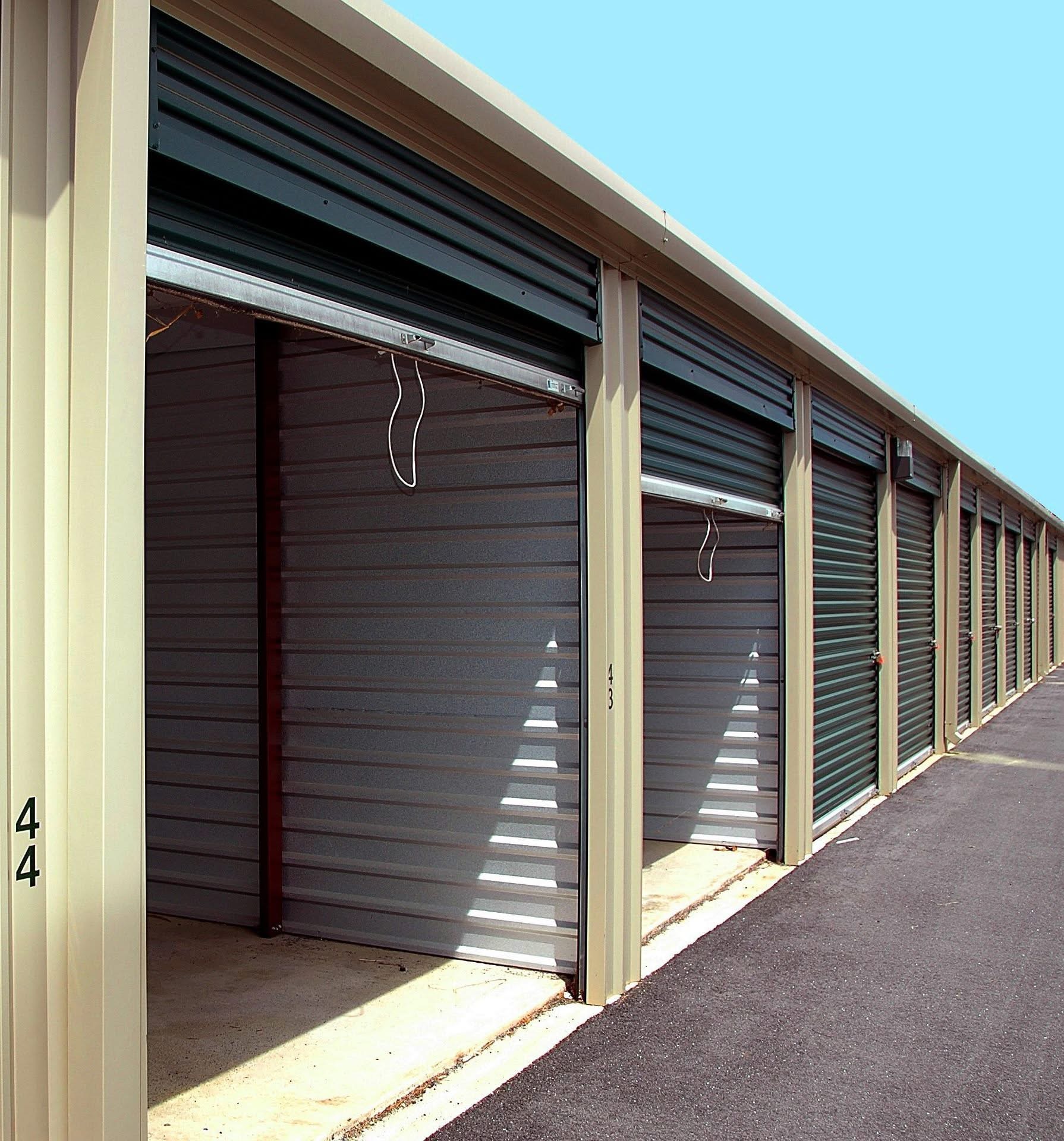 Row of steel mini-storage units with roll-up doors along a paved drive aisle