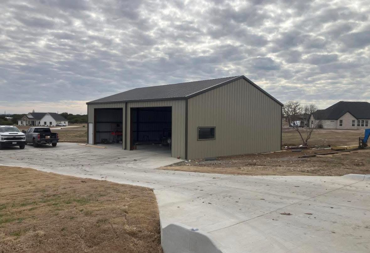 Two-bay tan metal garage and shop building with open doors and concrete driveway