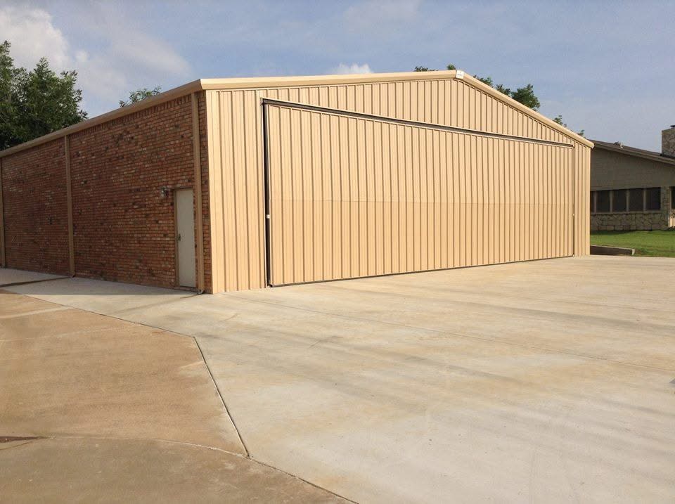 Tan metal hangar with brick wainscot and large sliding door for aircraft access