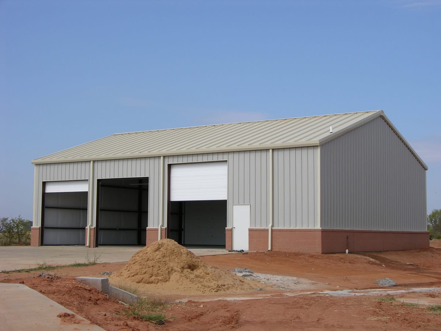 Gray gable steel building with brick wainscot under construction on a dirt lot