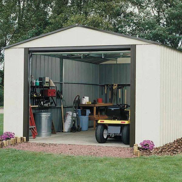 White metal storage shed with roll-up door and riding mower stored inside