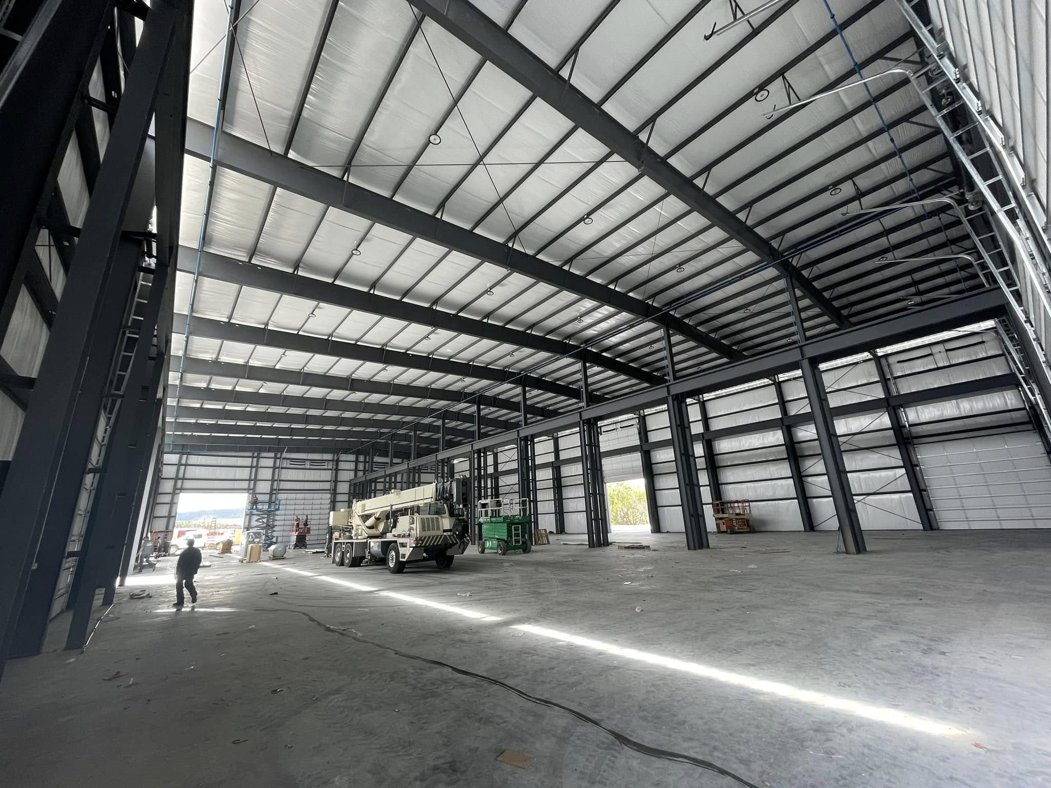 Interior of a large steel warehouse under construction with a mobile crane and scissor lifts on site